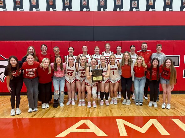 Large group posing in a gymnasium, wearing red and white team uniforms with a red-and-black wall behind them