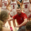 Basketball coach in red instructing players in white Broncos uniforms during a timeout