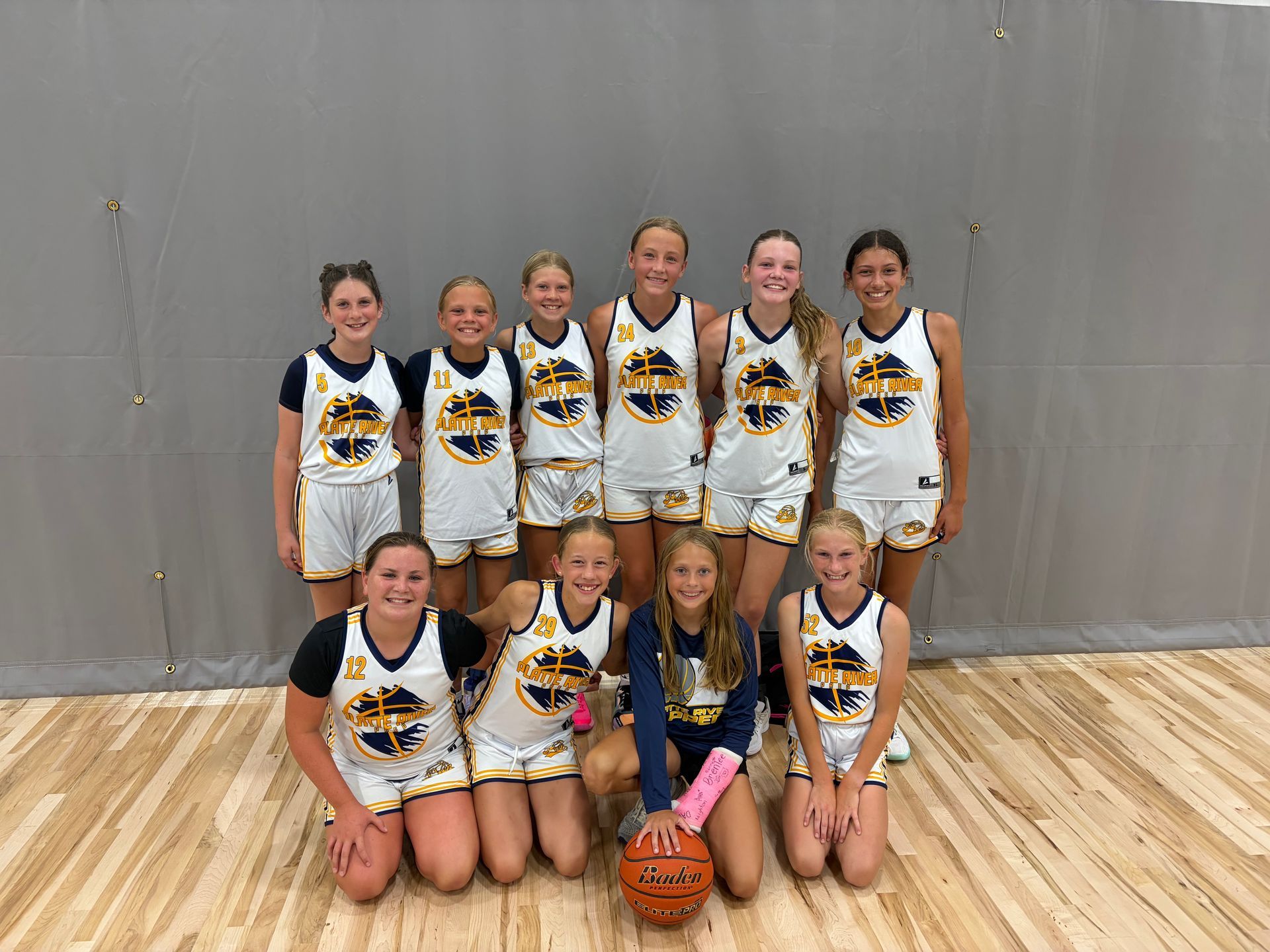 Group of athletes posing in a gym, standing and kneeling in rows on a basketball court.