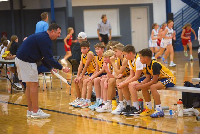 Basketball coach talking to seated youth players on a gym bench during a timeout