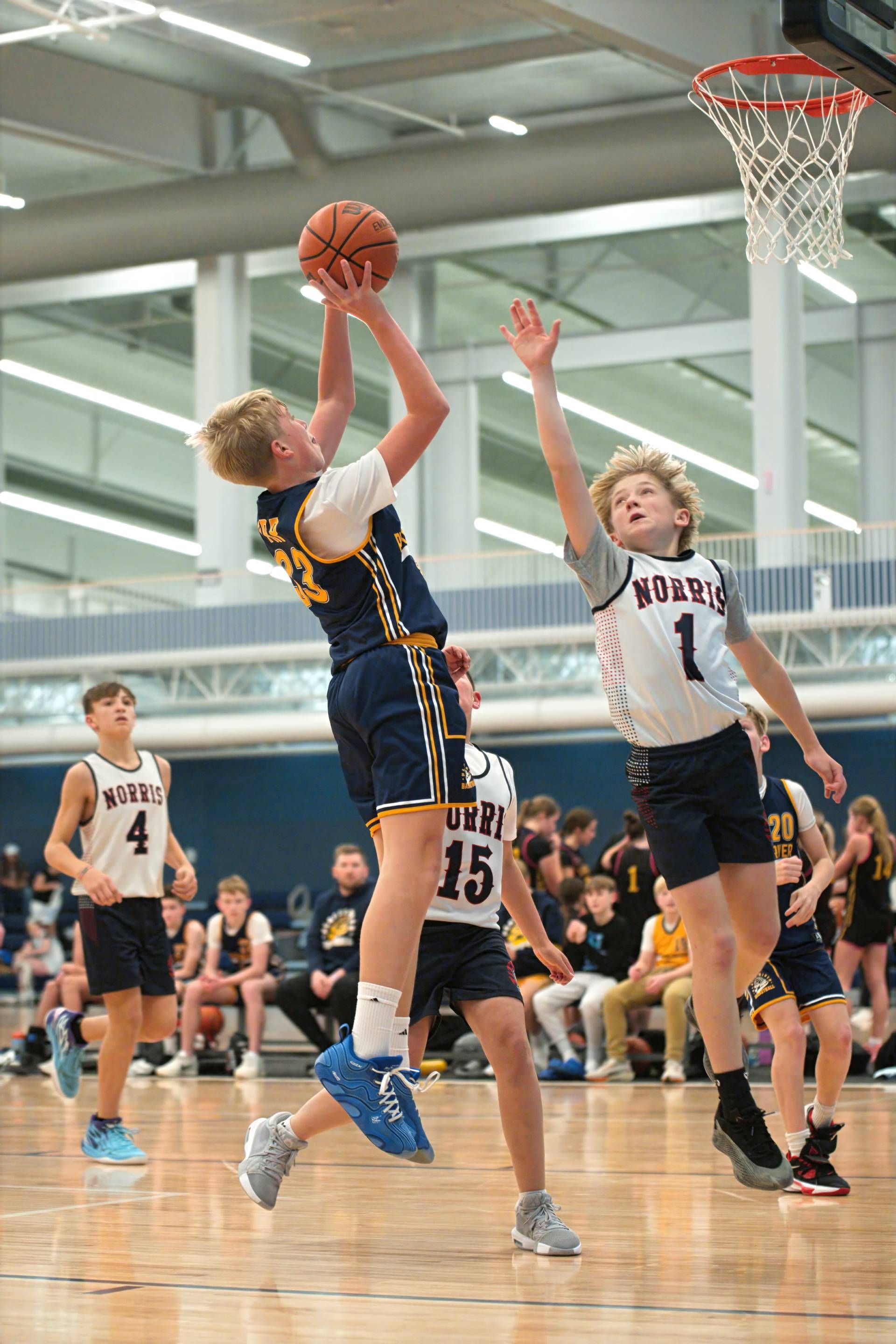 Two basketball players jump for a shot near the hoop in an indoor gym.