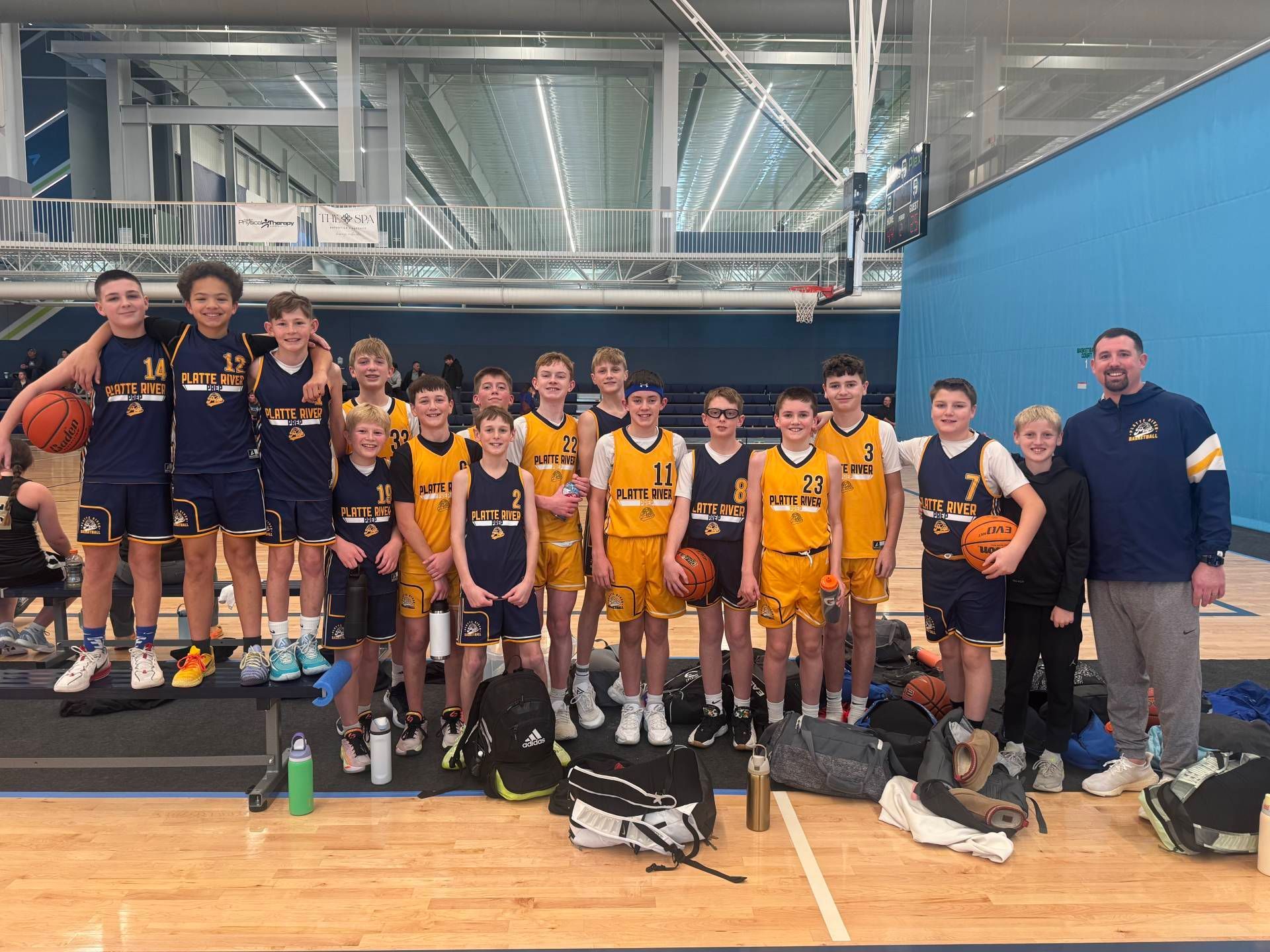 Youth basketball team posing with trophies in a gym, wearing navy and gold uniforms.
