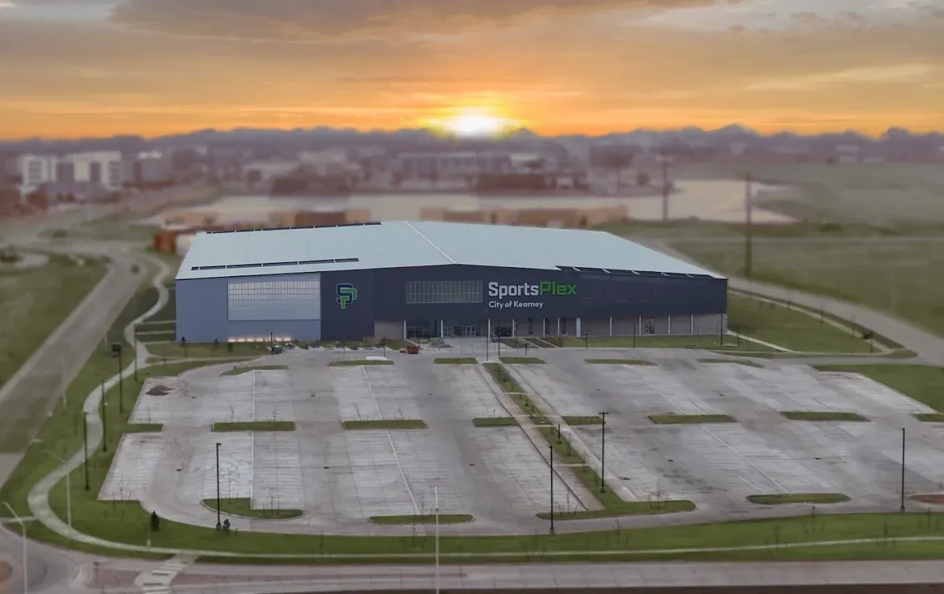 Aerial view of a large warehouse and empty parking lot at sunrise, with a city skyline in the distance.