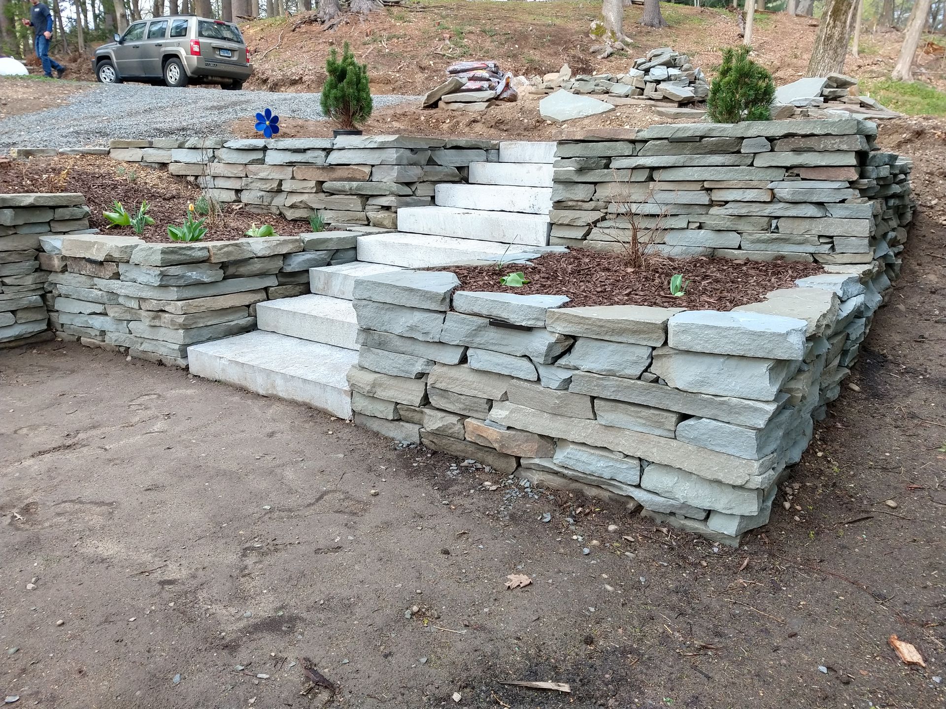 Stone steps and retaining walls in an outdoor setting, with a parked car in the background.