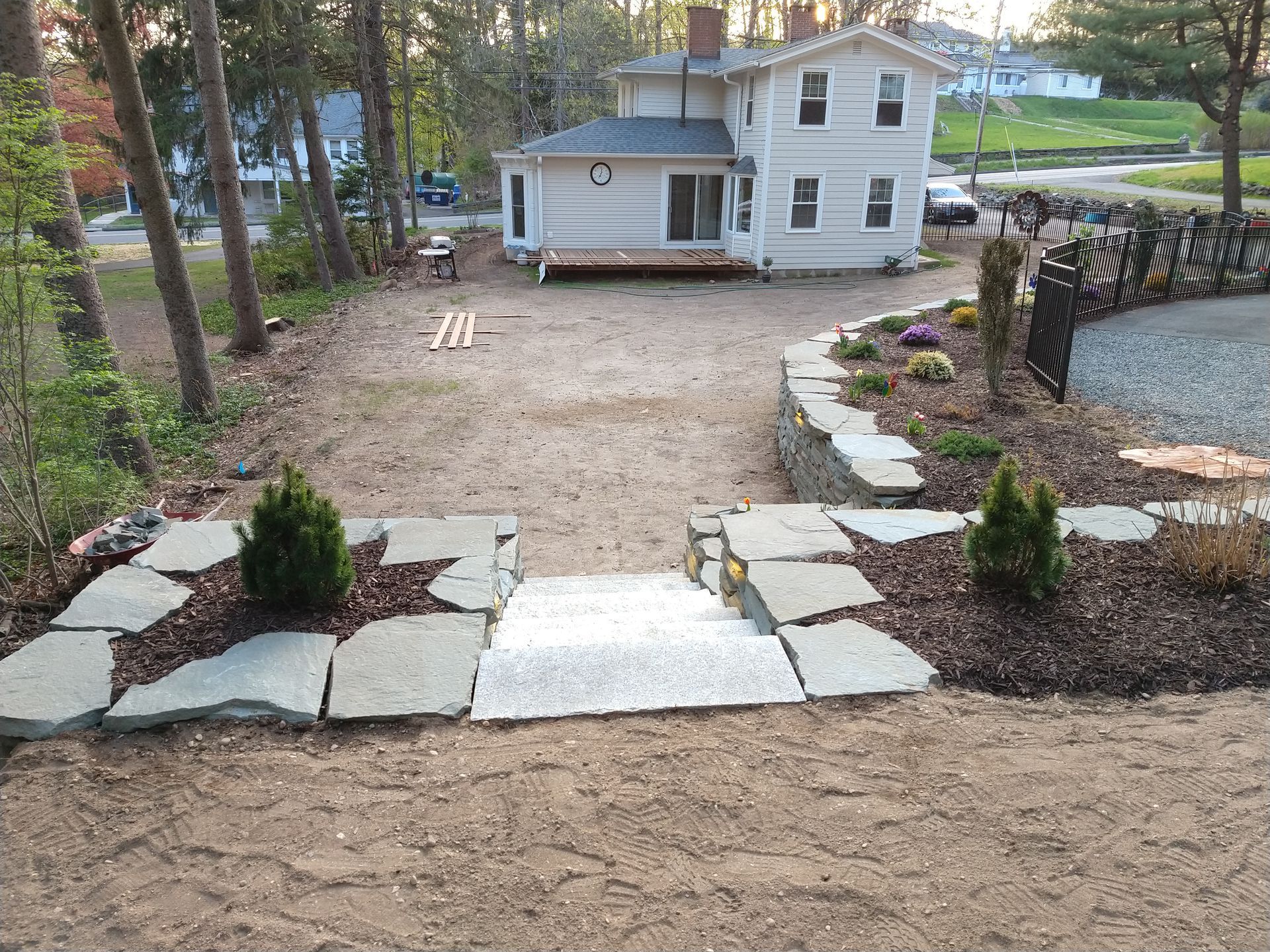 Stone steps lead to a light-colored house; landscaping features stone and mulch, with trees nearby.