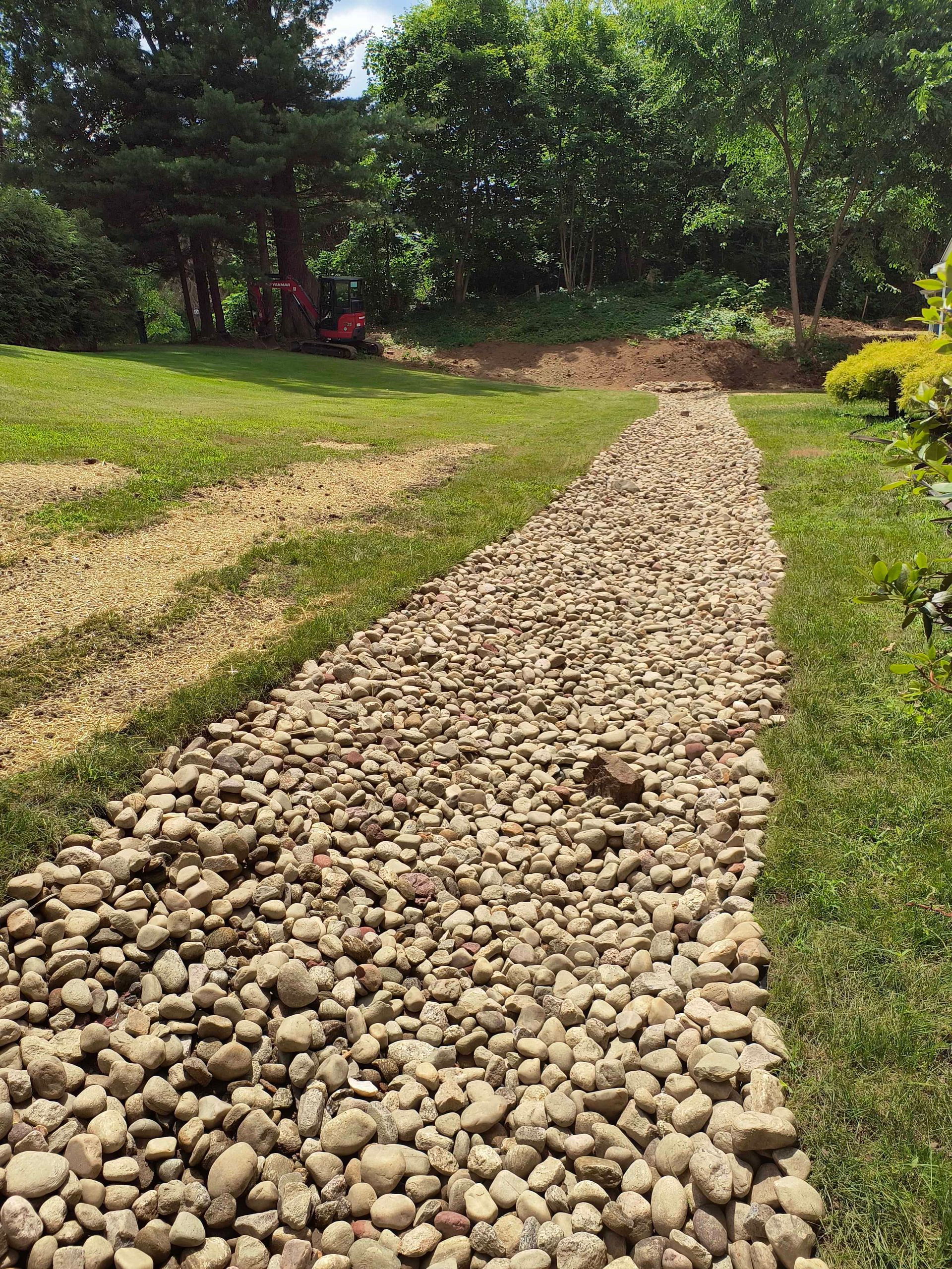 Stone path through green lawn, leading towards trees in sunny outdoor setting.