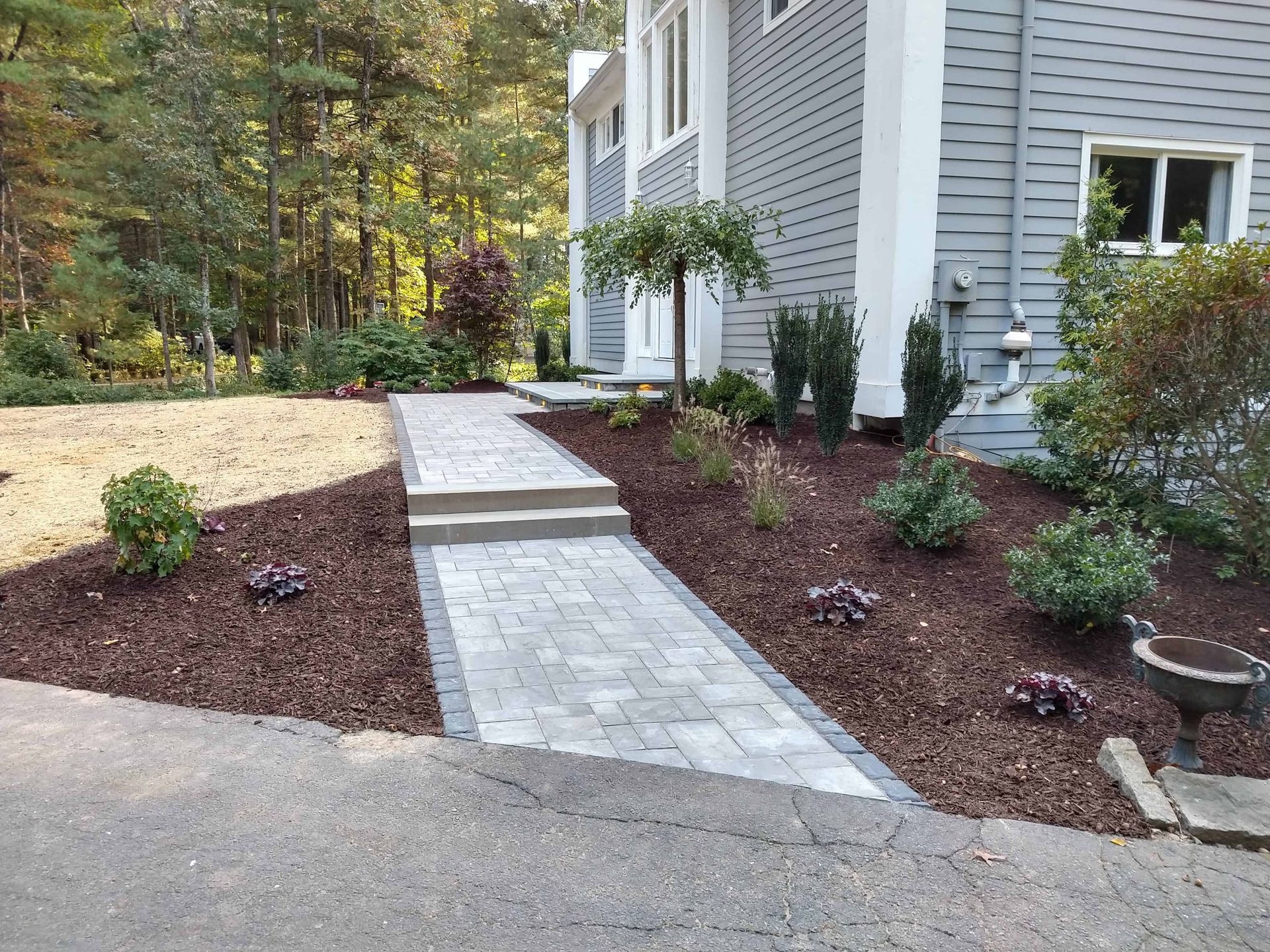 A paved walkway leads to a two-story house with landscaping and trees.