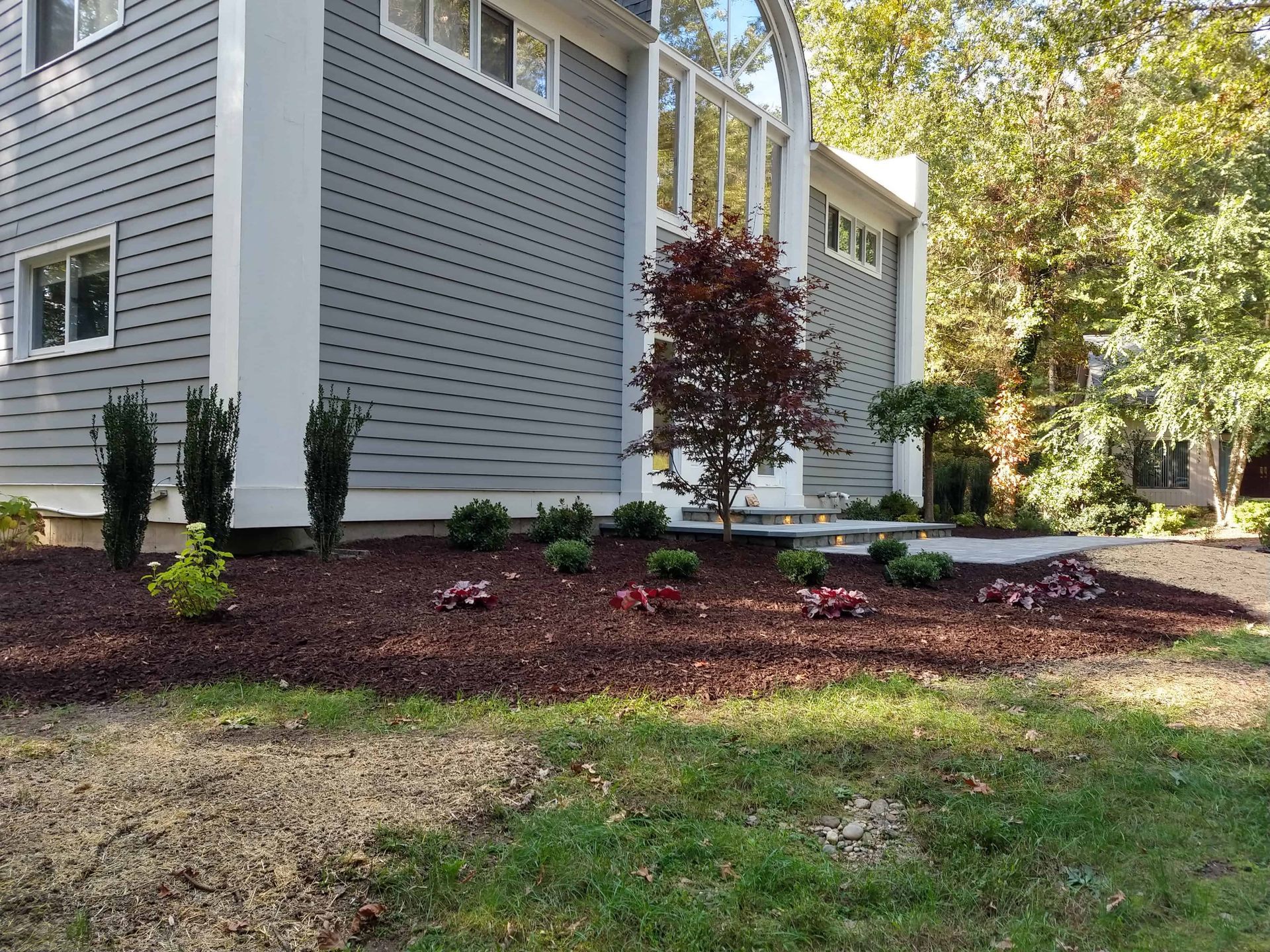 Gray house with landscaping featuring a red mulch bed and small plants.