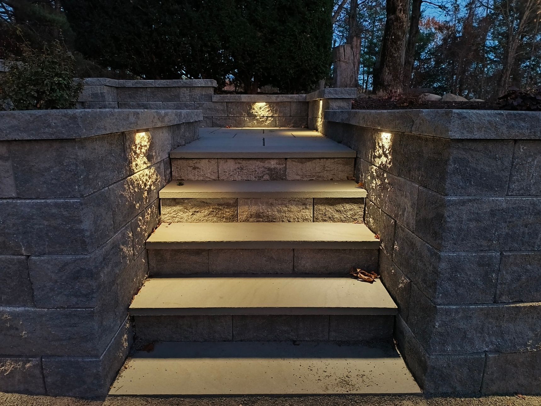 Stone steps lead to a light-colored house; landscaping features stone and mulch, with trees nearby.
