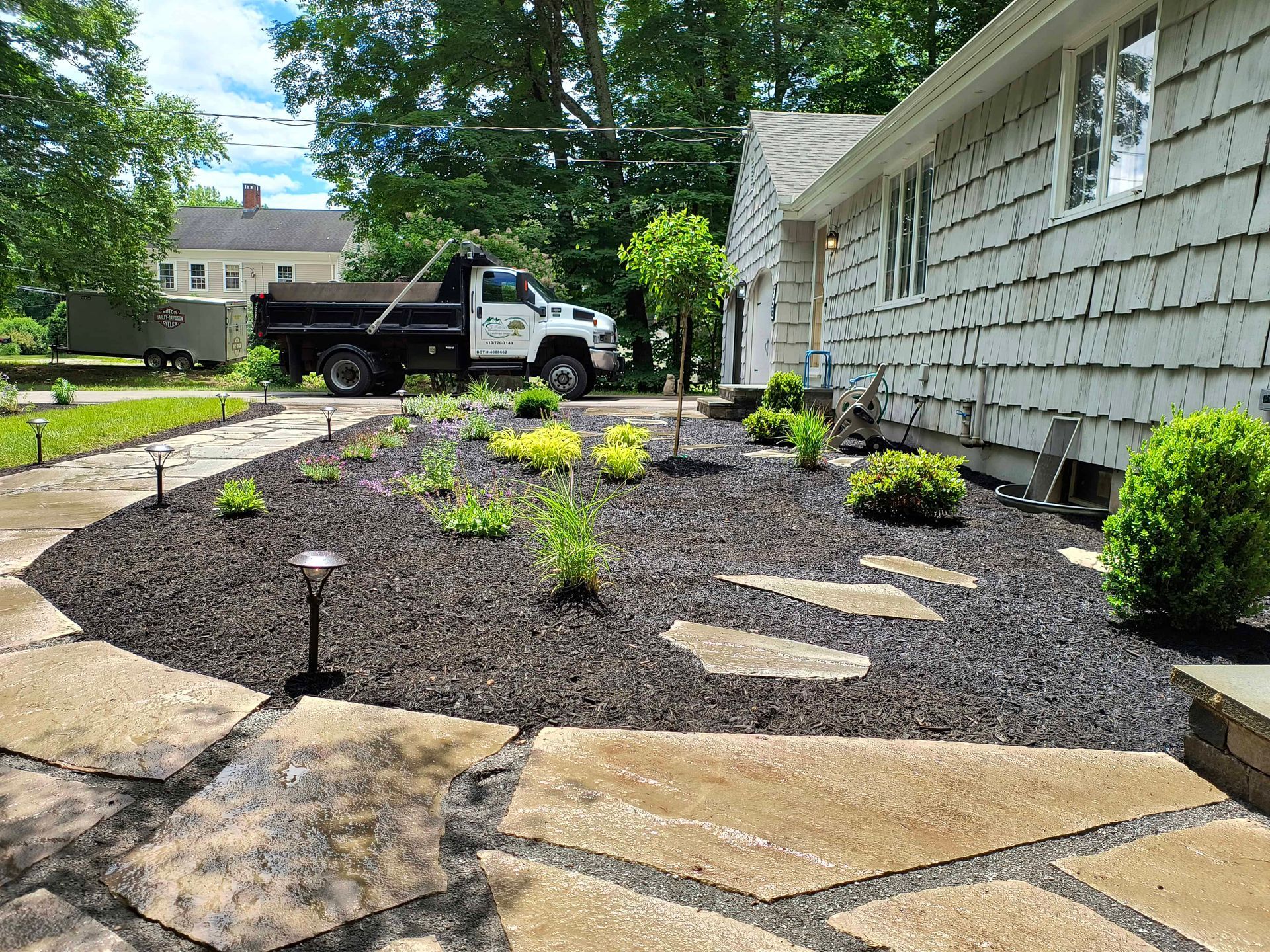 Landscaped yard with flagstone path, dark mulch, and truck in the background.