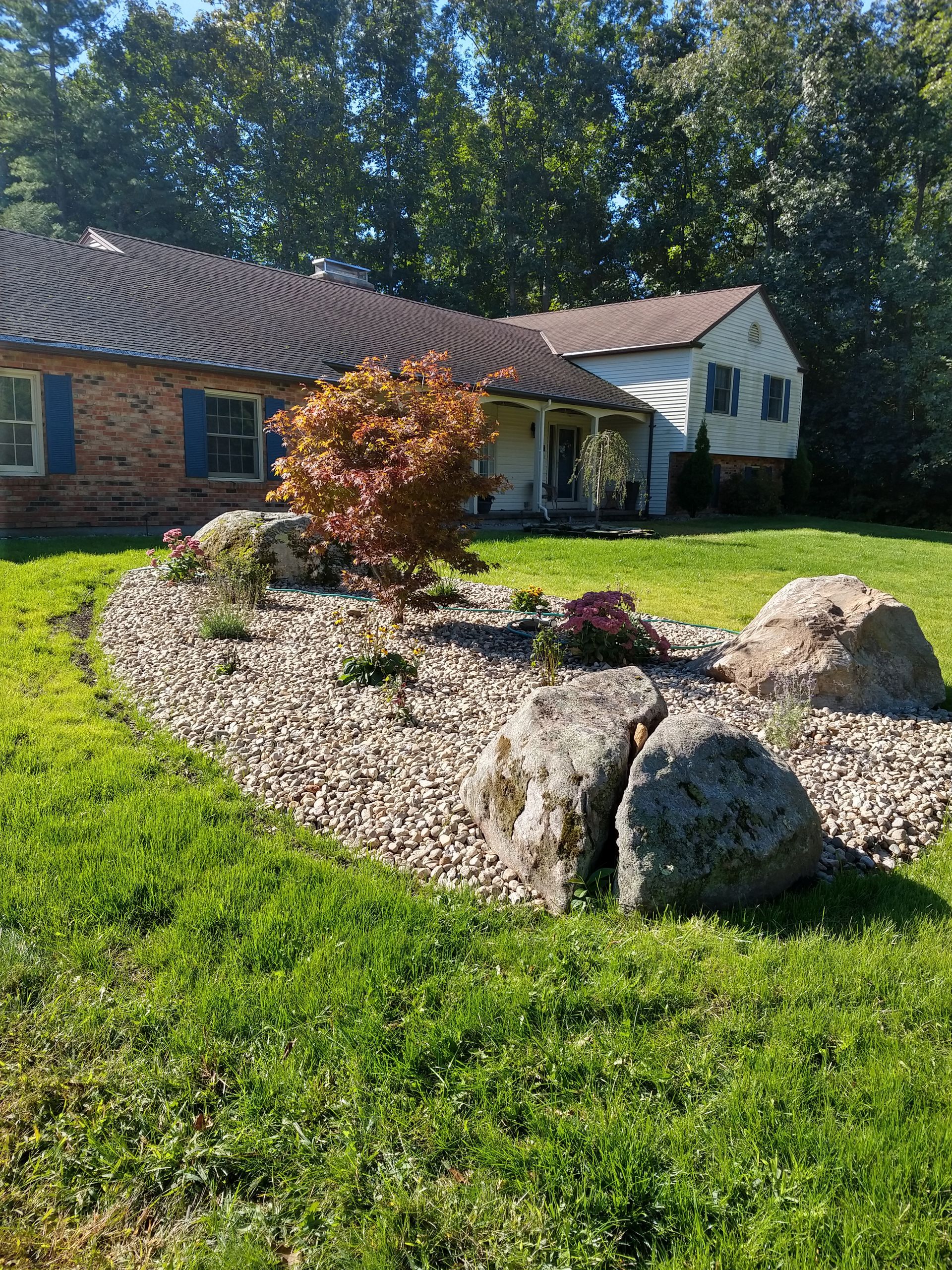 A brick house with a front yard rock garden. The garden has a small tree and is surrounded by grass.