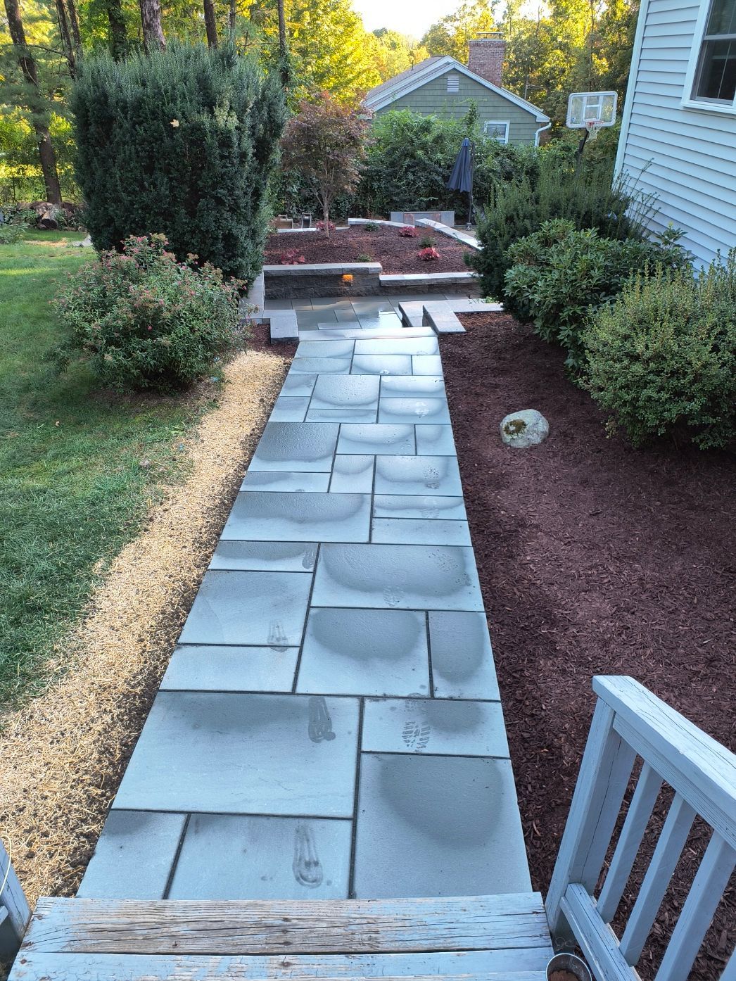 Stone walkway leading to a house, with shrubs and mulch on either side.