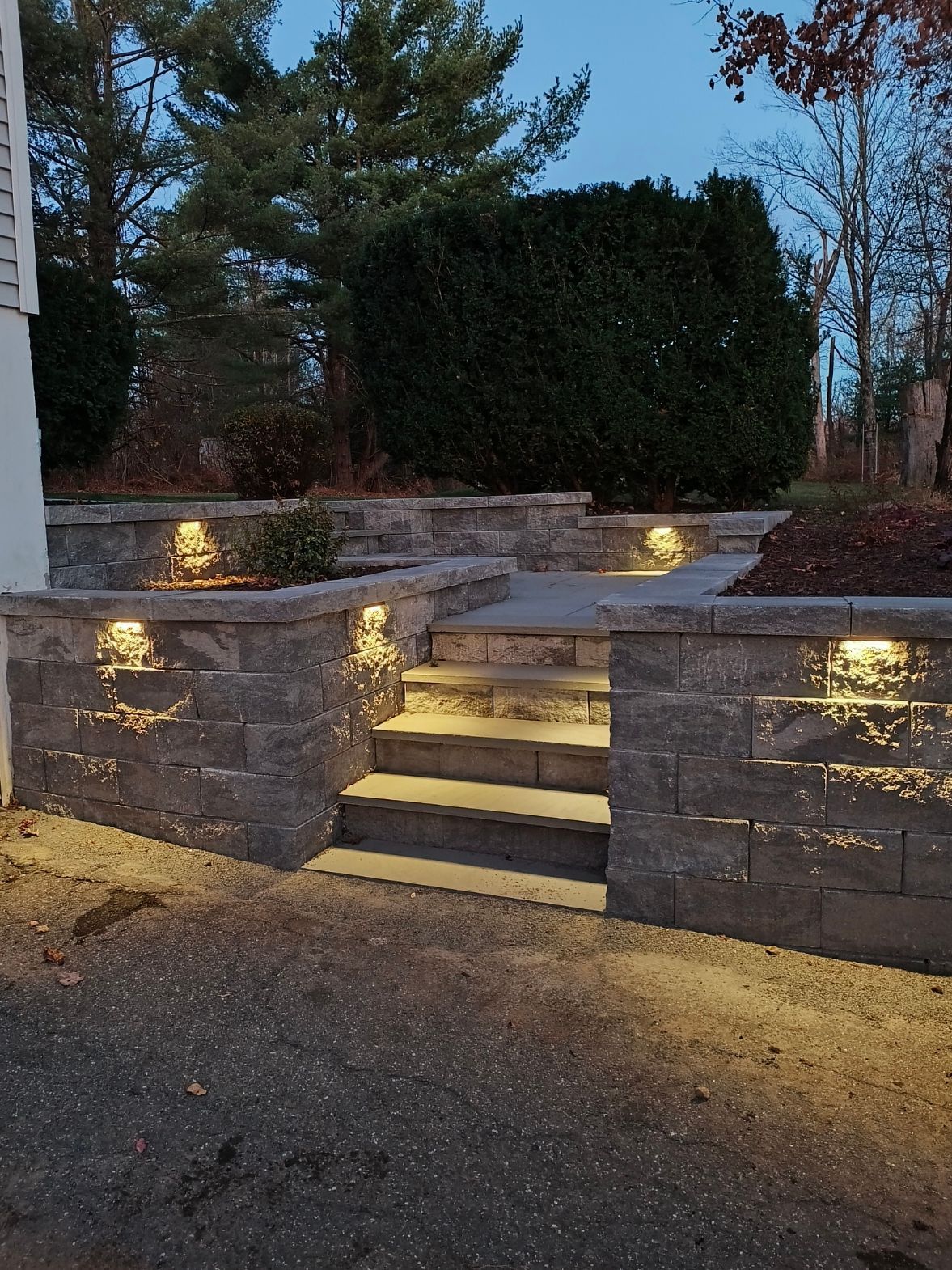 Stone steps with built-in lights leading up to a patio. Dark gray blocks, nighttime setting.