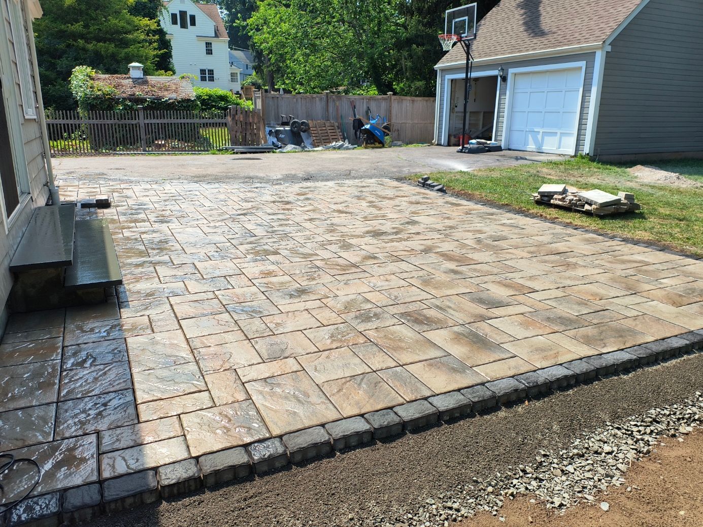 Paver patio with a dark border, next to a building and grass.