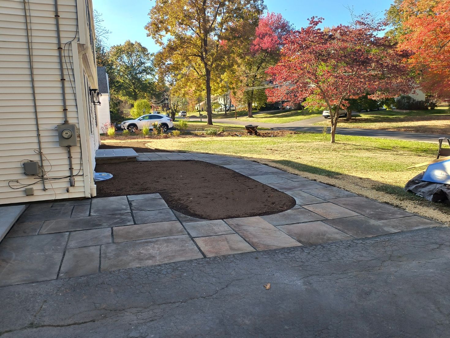 Stone path next to a house and a brown mulch area surrounded by grass and trees with fall foliage.