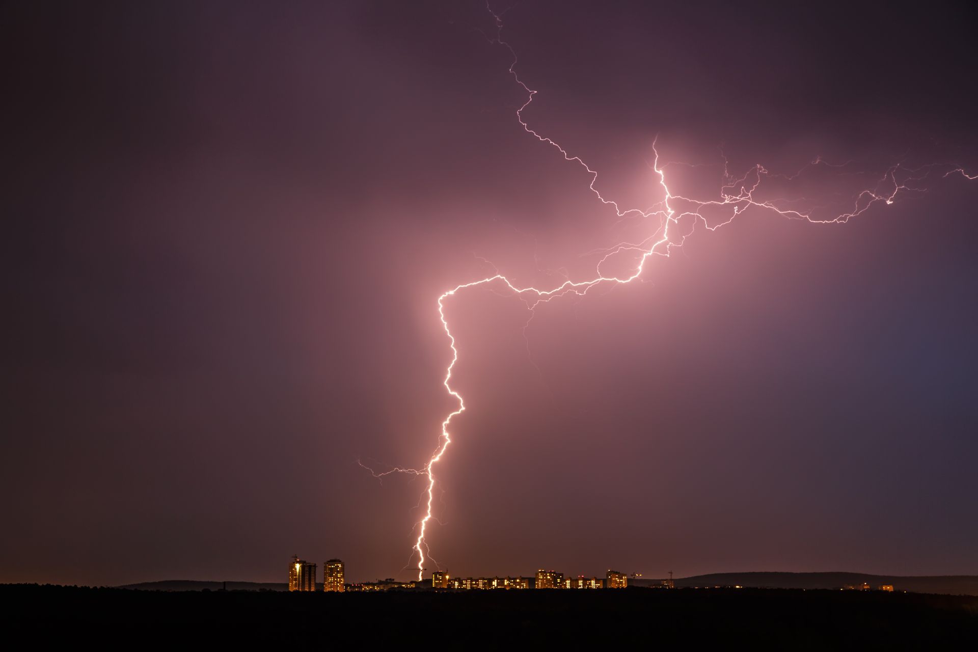 Lightning strike over a city skyline during a nighttime thunderstorm with dramatic purple storm clou