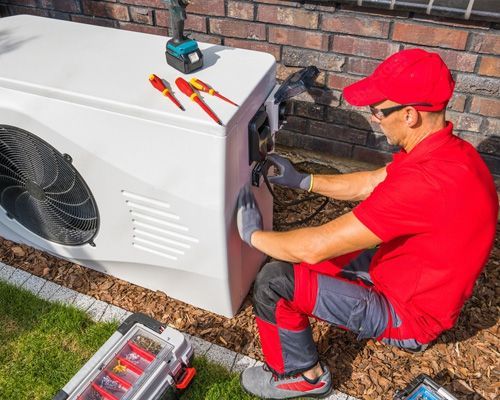 A man in a red shirt is working on a heat pump.
