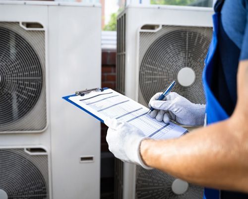 Arctic Fox technician is writing on a clipboard in front of air conditioners.