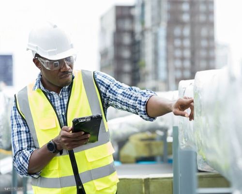 A man in a hard hat and safety vest is looking at a tablet.