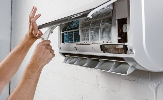 A person is cleaning an air conditioner with a brush.