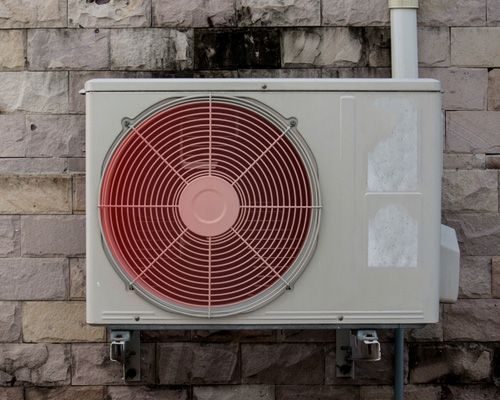 A white air conditioner with a red fan attached to a brick wall.