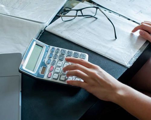 A person is using a calculator on a desk.