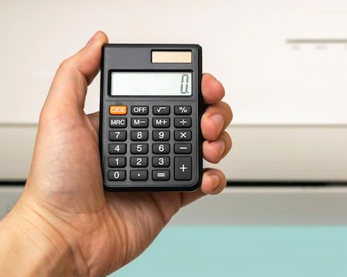 A person is holding a calculator in their hand in front of an air conditioner.