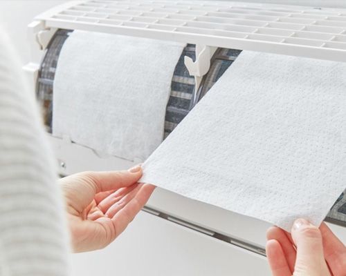 A person is holding a piece of paper in front of an air conditioner.