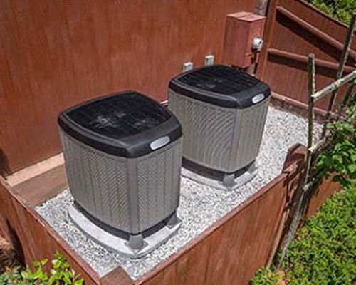 Two air conditioners are sitting on top of a wooden fence.