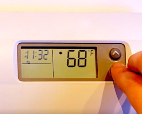 A person is adjusting a digital thermostat to 68 degrees