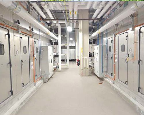 A long hallway in a building with a lot of pipes and doors.