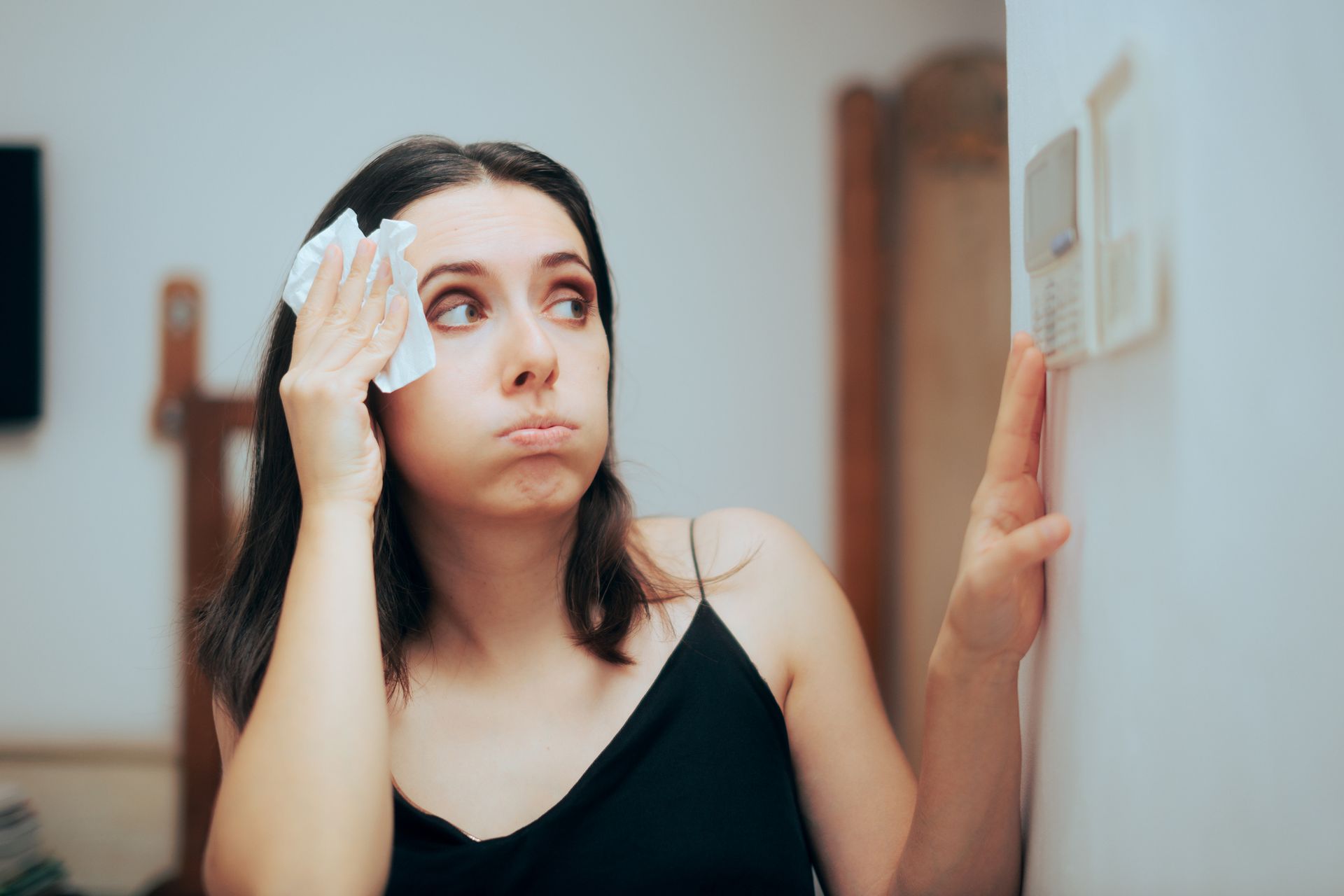 Homeowner adjusting a thermostat during summer while using a whole-home dehumidification system.