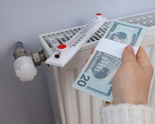 A person is holding a stack of money in front of a radiator.