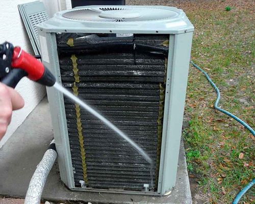 A person is cleaning an air conditioner with a hose