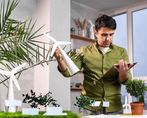 A man is holding a model of a windmill while using a tablet.