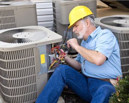 Arctic Fox technician is sitting on the ground working on an air conditioner.