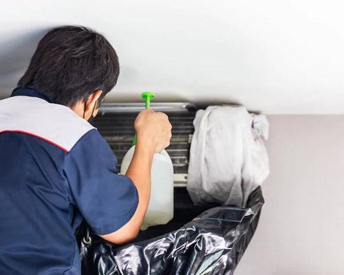 A man is cleaning an air conditioner with a spray bottle.