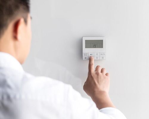 A man is adjusting the temperature on a thermostat.