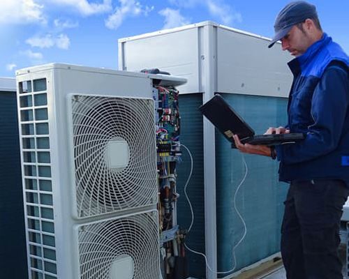 A man is working on an air conditioner while holding a laptop.