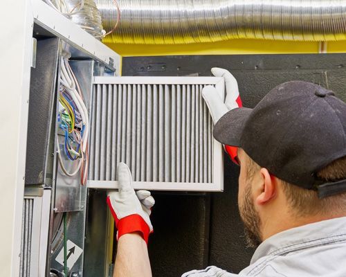 A man is holding a filter in his hand while working on an air conditioner.