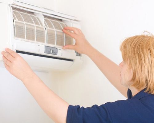 A woman is cleaning the filter of an air conditioner.