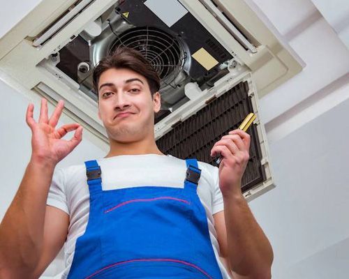 A man in blue overalls is working on an air conditioner.