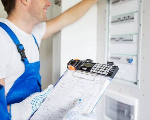 A man in blue overalls is holding a clipboard and a calculator.