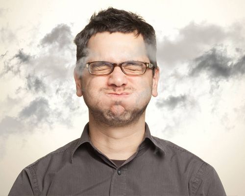 A man wearing glasses is making a funny face with smoke coming out of his mouth.