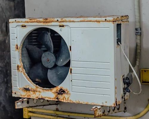 An old rusty air conditioner is hanging on a wall.