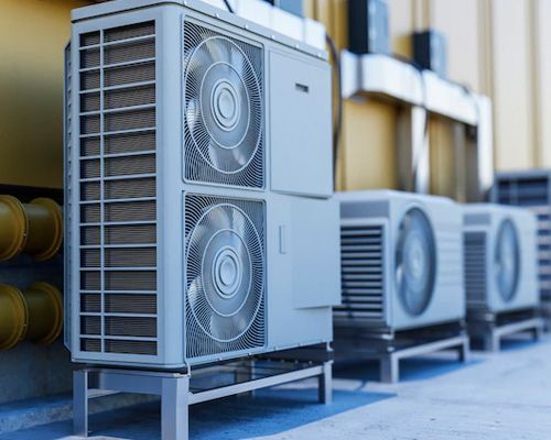 A row of air conditioners are sitting outside of a building.