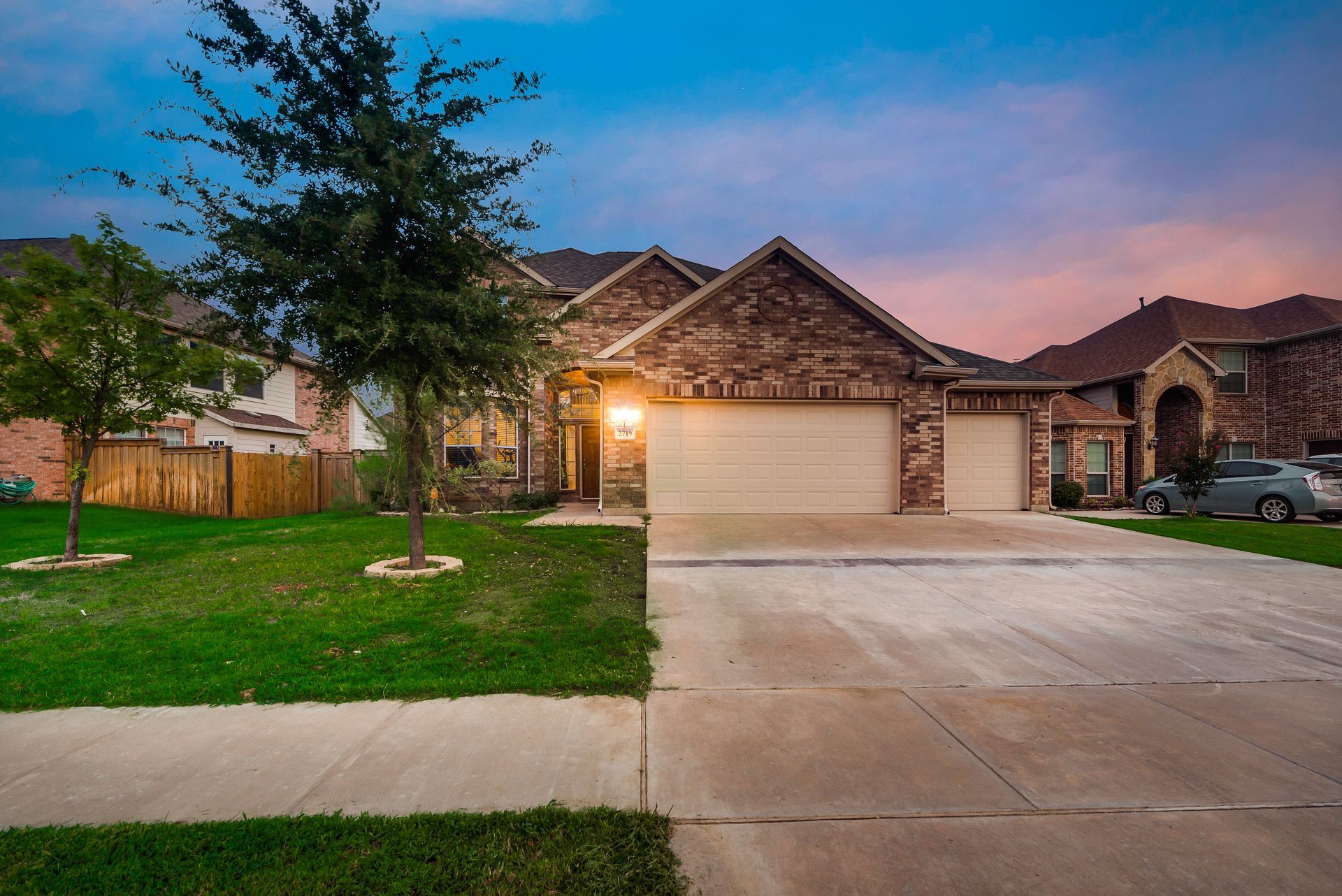 Brick house with a two-car garage, green lawn, and blue twilight sky.