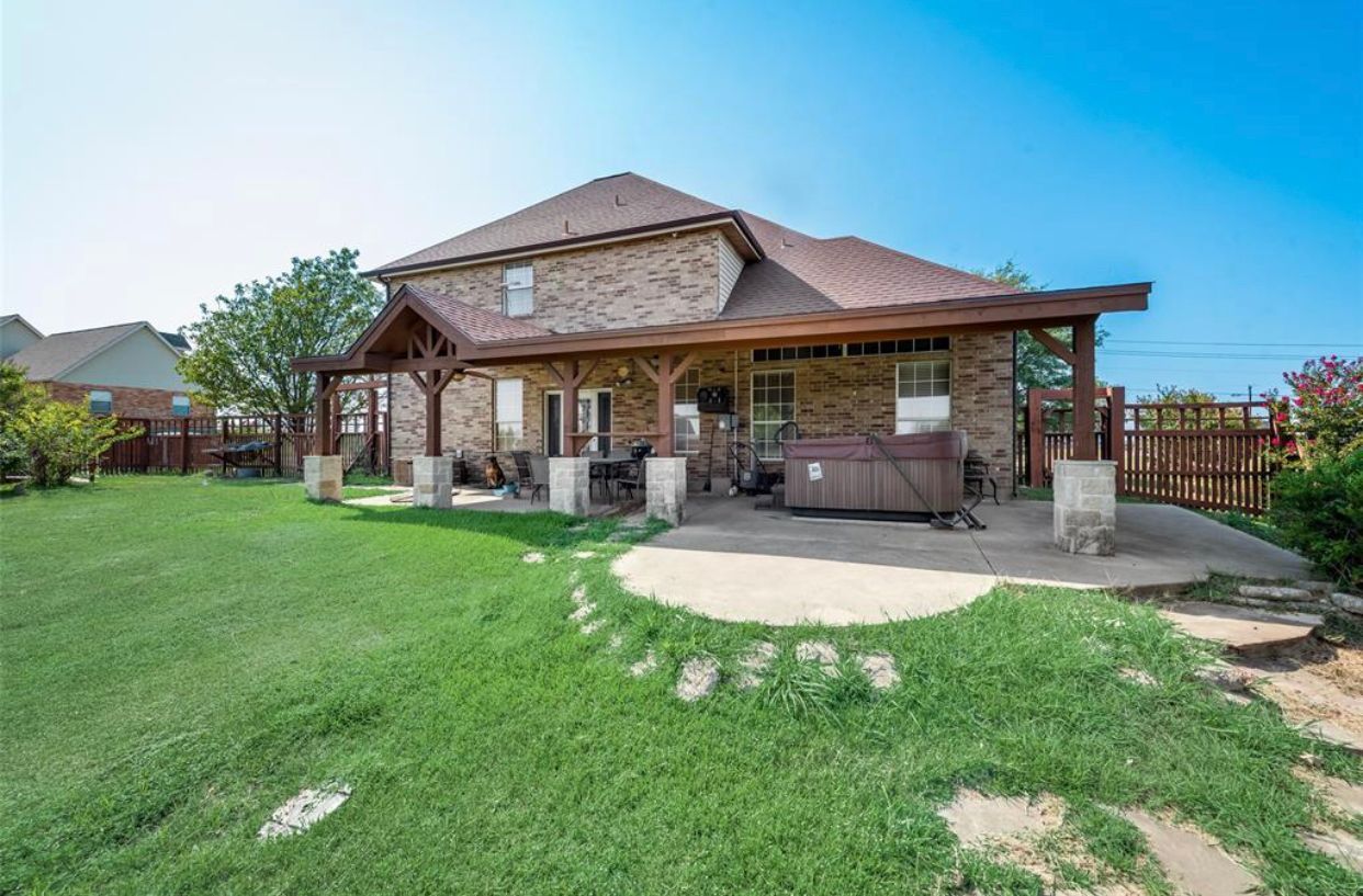 Brick house with covered patio, backyard, and hot tub.