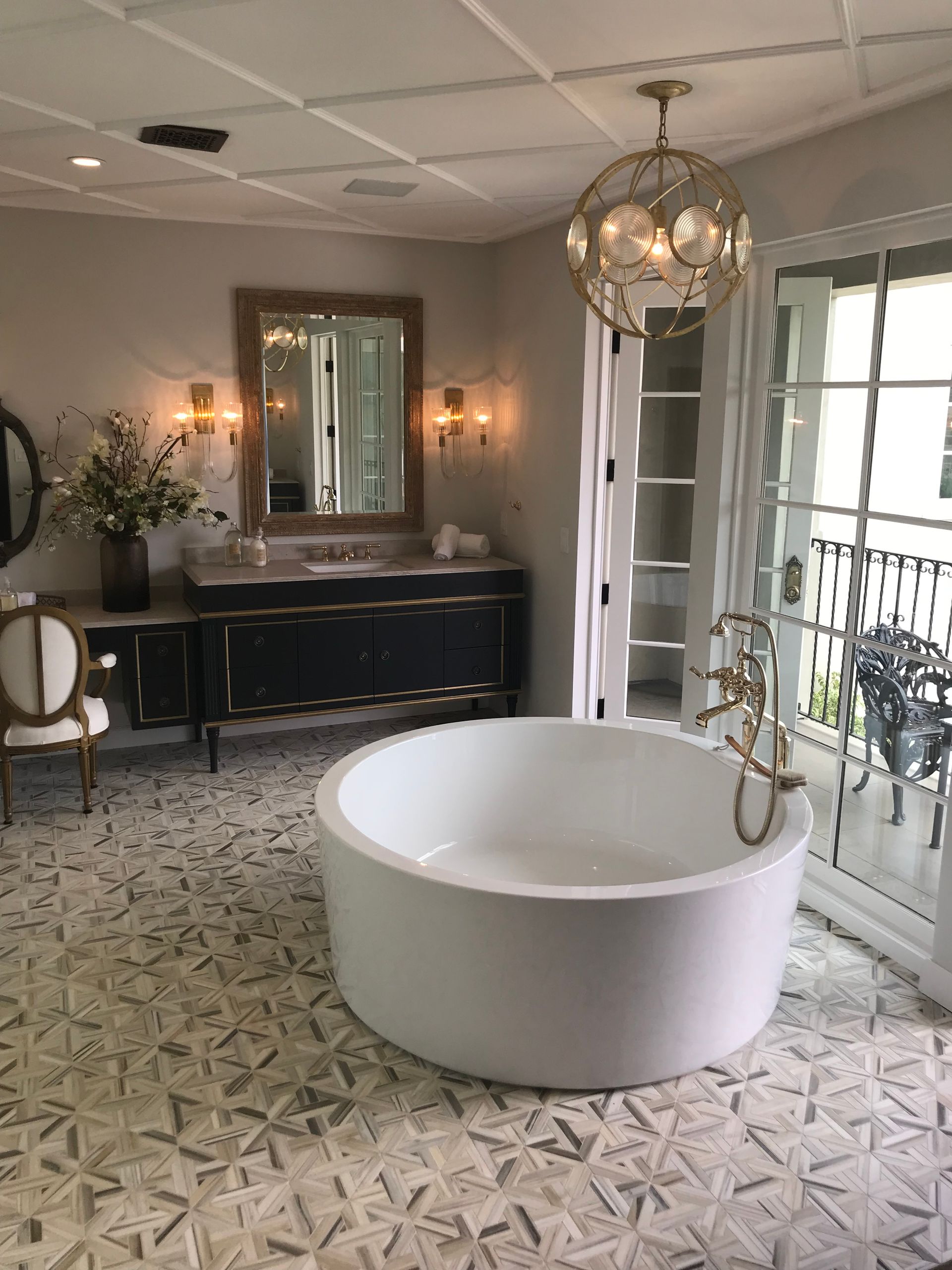 Elegant bathroom with a round white tub, ornate light fixture, and balcony access.