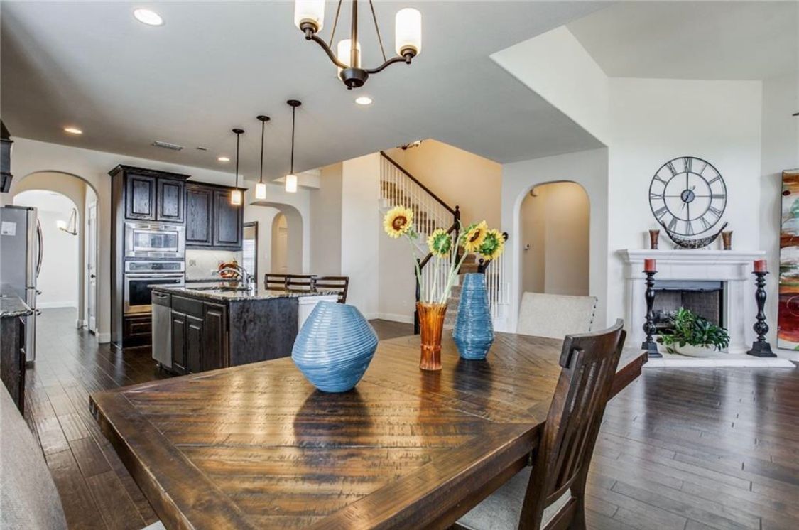 Dining room with a wooden table, kitchen, fireplace, and stairs.